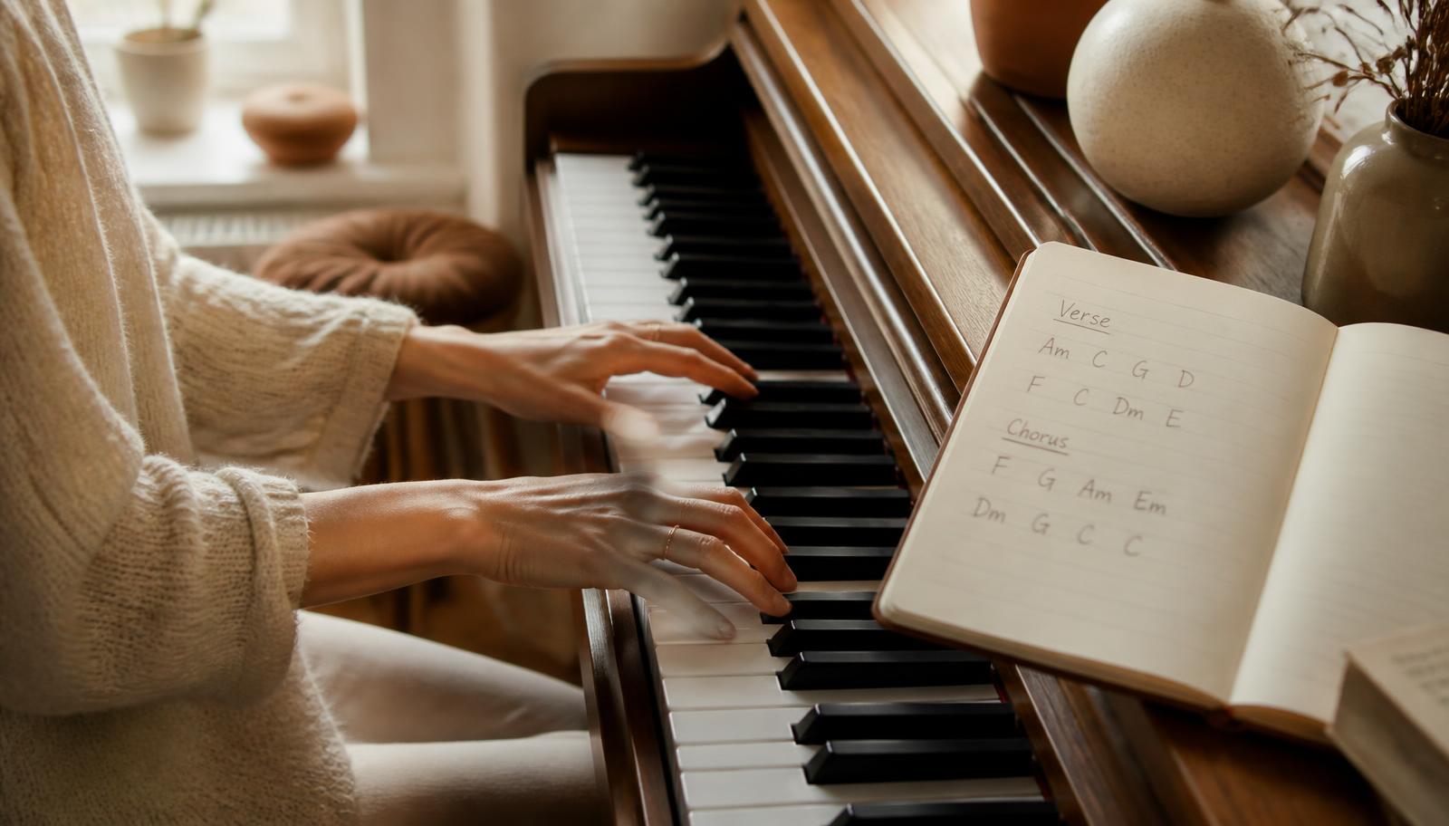Hender som spiller akkorder på et piano med en notatbok med akkordsymboler ved siden av